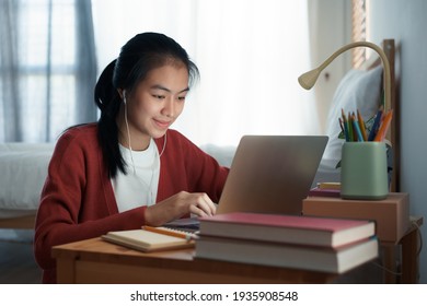 Asian woman video call online via the internet tutor on a computer laptop with headphone, Asia girl is studying while sitting in the bedroom at night. Concept online learning at home 