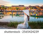 Asian woman in Vietnamese national costume and long-tail boat decorated with Vietnamese paper lanterns on the river at night, a beautiful and important tourist attraction in Vietnam, Hoi An, Vietnam.