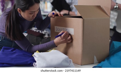 Asian woman volunteer write donation on cardboard box working in non-profit organization. Social workers sort and pack goods for charity - Powered by Shutterstock