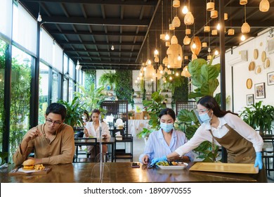 Asian Woman Waering Mask And Asian People Eating Food Alone At Table With Plexi Screen Between Table In Reopening Restaurant After Lockdown Measure.