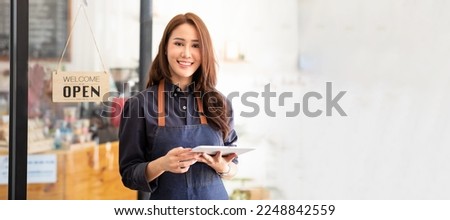 The Asian woman is a waitress in an apron, the owner of the cafe stands at the door with a sign Open waiting for customers. Small business concept, cafes and restaurants 