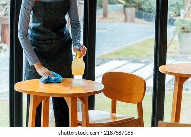 Asian Woman Waitress Staff In Apron Cleaning Table With Disinfectant Spray For Protect Infection Coronavirus (covid-19) In Cafe Coffee Shop Restaurant. Hotel Clean Service, New Normal Concept