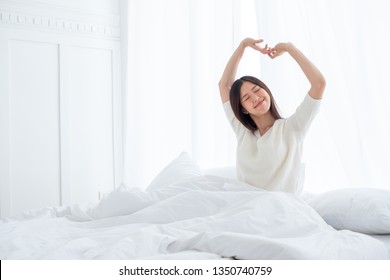 Asian Woman Wake Up In The Morning, Sitting On White Bed And Stretching, Feeling Happy And Fresh