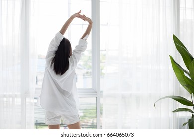 Asian woman waking up in her bed fully rested and open the curtains in the morning to get fresh air. - Powered by Shutterstock