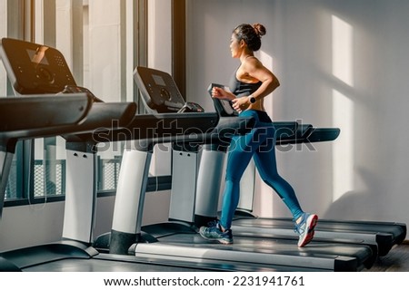 Asian woman walk and running on treadmills in the morning at gym.she wear black sport bra and blue plant.Bodybuilding and sport healthy lifestyle concept.