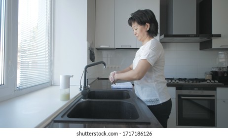 Asian woman washes hands with soap in the kitchen