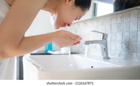 Asian woman washing her face with cold water at bathroom sink. Wash your face once in the morning and once at night, as well as after sweating heavily.
