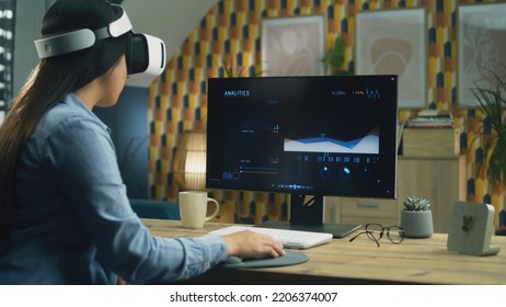 Asian Woman Watching Analytic Graphics On Personal Computer Using Modern VR Glasses While Sitting At The Table At Home Office