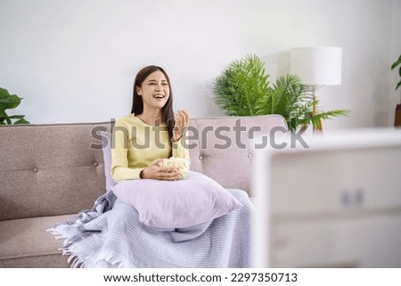 Asian woman Watching smart TV and using remote controller Hand holding television audio remote control at home with popcorn