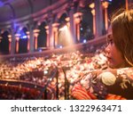 An asian woman watching a west end show with blurred crowds of seated people in background