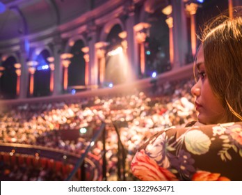 An Asian Woman Watching A West End Show With Blurred Crowds Of Seated People In Background