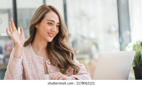 Asian Woman Waving Hello Talking On A Video Call. Successful Young Woman Sitting At Business Workspace. Business Conference Via Laptop.