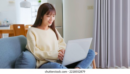 Asian Woman Wear Hoodie Sitting On The Couch Using Laptop In Living Room At Home During Winter