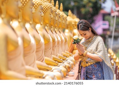 Asian Woman Wearing Ancient Thai Traditional Dress Holds Garland And Fresh Flowers Paying Homage  Buddha In Temple To Make A Wish On The Traditional Songkran Festival In Thailand.