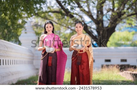 Asian woman wearing ancient Thai traditional dress homage Buddha hold silver bowl in temple to make a wish on the traditional Songkran festival in Thailand.