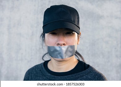 Asian Woman Wearing A Black Cap With Packing Tape Over Her Mouth