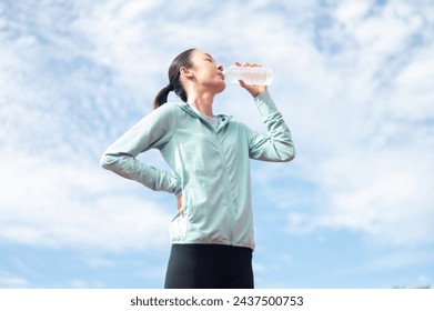 Asian woman wearing blue sportswear Stand and drink water after exercising. outdoor exercise Exercise in the stadium She is exercising and holding a water bottle. active living athletes drink water - Powered by Shutterstock