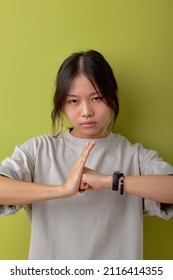 Asian Woman Wearing Casual T-shirt Having Serious Confident Look, Showing Clenched Fist. Feminism, Equality And Women's Liberation. Portrait Isolated Over Green Studio Background.