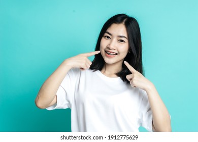 Asian Woman Wearing Dental Braces Pointing To Tooth Sample And Smiling With Her Healthy White Teeth Isolated Shot On Blue Background