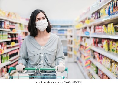 Asian woman wearing face mask and rubber glove push shopping cart in suppermarket departmentstore. Girl choosing, looking grocery things to buy at shelf during coronavirus crisis or covid19 outbreak. - Shutterstock ID 1695585328