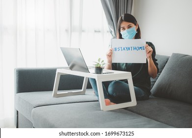 Asian Woman Wearing Face Mask Working At Home During Coronavirus Quarantine Showing Stay At Home Sign