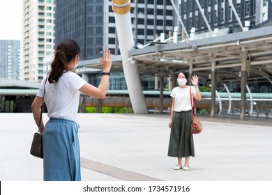 Asian Woman Wearing Face Mask Standing Apart On The Sky Walk In City And Say Hi To Each Other As A Social Distance Guideline During Covid-19 Or Coronavirus Outbreak. New Normal Lifestyle Concept