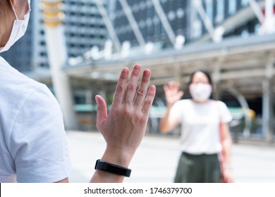 Asian Woman Wearing Face Mask Standing Apart On The Sky Walk In City And Say Hi To Each Other As A Social Distance Guideline During Covid-19 Or Coronavirus Outbreak. New Normal Lifestyle Concept