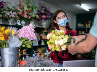 Asian Woman Wearing  Face Mask Or Protective Mask Against Coronavirus Crisis, Florist Owner Of A Small Florist Business Holding Flowers For Delivery To Customers At Her Store