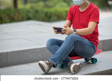 Asian woman wearing face mask sit on skateboard using smartphone in modern city - Powered by Shutterstock