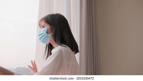 asian woman wearing face mask stays isolation at home for self quarantine due to epidemic of COVID19 - she looks out the window - Powered by Shutterstock