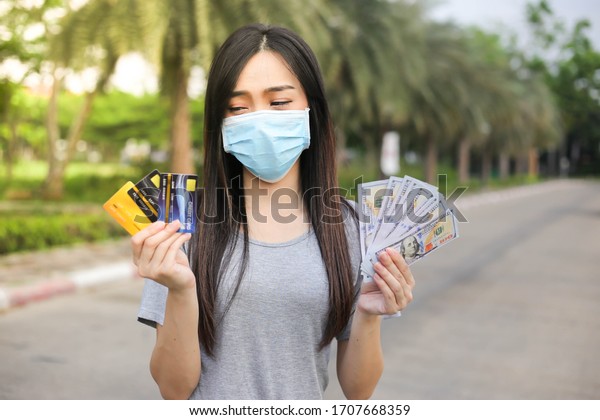 Asian woman  wearing face\
protection ,Virus mask  Holding money and credit card financial\
problem,economic depression during the Coronavirus,Covid-19\
pandemic