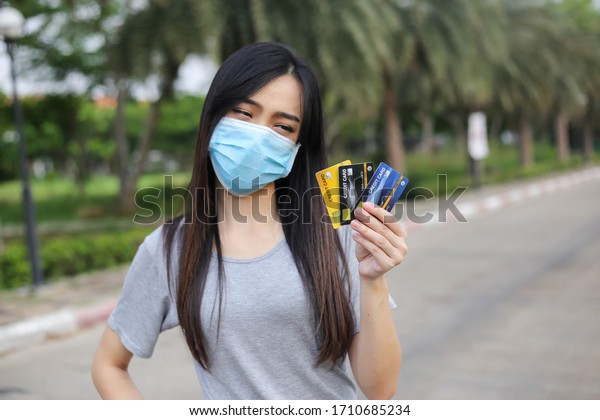 Asian woman  wearing face\
protection ,Virus mask  Holding money and credit card financial\
problem,economic depression during the Coronavirus,Covid-19\
pandemic