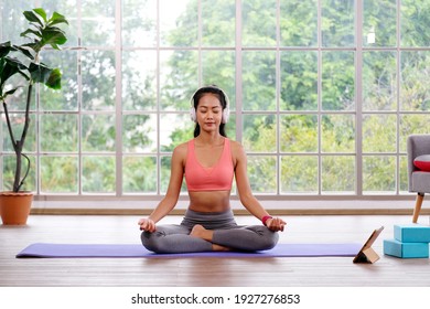 Asian Woman Wearing Headphones While Practice Yoga Meditation Exercise At Home, Young Asia Female Sitting On Mat For Relaxed Yoga Posture , Exercise At Home, Wellbeing, Mental Health