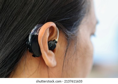 Asian woman wearing hearing amplifier to assist her hearing deafness problem, close up. 