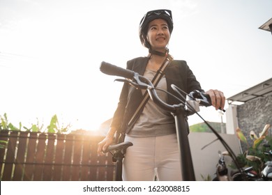 asian woman wearing helmet and bag prepares a folding bike from her home for go to work to the office