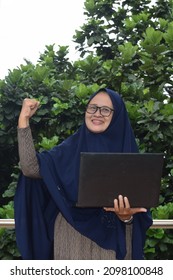 Asian Woman Wearing Hijab Holding A Laptop Happily. Selective Focus.