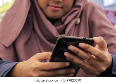 Asian Woman Wearing Hijab. Using Her Smartphone. Blurry Mall Background.