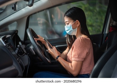 Asian Woman Wearing A Mask In The Car She Uses Her Mobile Phone To Check Information About The COVID-19 Outbreak.