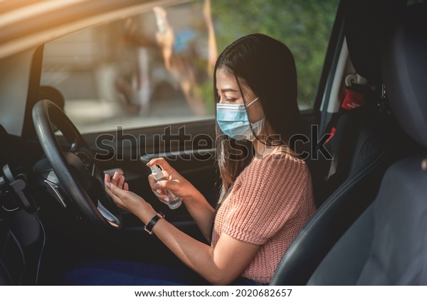 Asian woman wearing\
a mask in the car Use hand spray before driving to prevent the\
spread of covid-19 virus.