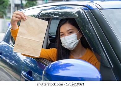 Asian Woman Wearing Mask And Holding Paper Bag Of Fast Food Through The Window Car. Drive Thru Food Service Concept