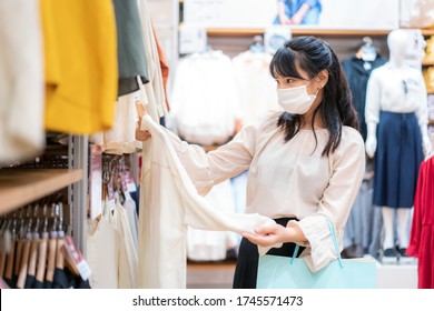 Asian Woman Wearing Mask Over Her Face While Choosing Shirt At Shopping Mall With Shopping Bag For Healthcare And Prevention From Coronavirus, Covid19 Influenza In Crowded Place.
