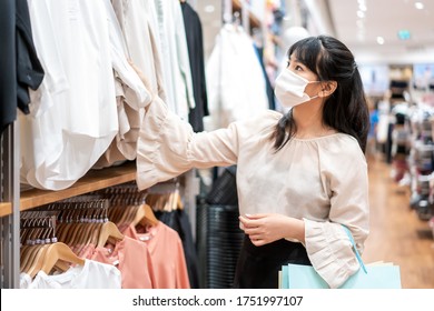 Asian Woman Wearing Mask Over Her Face While Choosing Shirt At Shopping Mall With Shopping Bag For Healthcare And Prevention From Coronavirus, Covid19 Influenza In Crowded Place.
