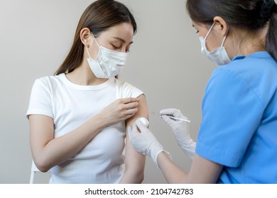 Asian woman wearing a medical mask receives coronavirus vaccine from a doctor. People are vaccinated against COVID-19 to prevent infection with the virus and stop its spread. - Shutterstock ID 2104742783