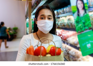 Asian woman wearing protective face mask hold paper shopping bag with fruits and vegetables in supermarket . Girl, looking grocery to buy  some fruit. New normal after covid-19. Family concept. - Shutterstock ID 1766156360