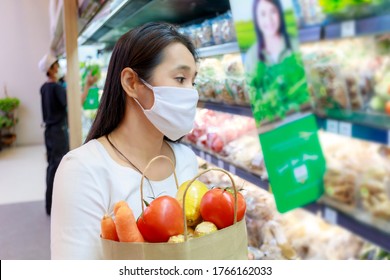 Asian Woman Wearing Protective Face Mask Hold Paper Shopping Bag With Fruits And Vegetables In Supermarket . Girl, Looking Grocery To Buy  Some Fruit. New Normal After Covid-19. Family Concept.