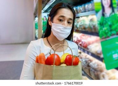 Asian woman wearing protective face mask hold paper shopping bag with fruits and vegetables in supermarket . Girl, looking grocery to buy  some fruit. New normal after covid-19. Family concept. - Shutterstock ID 1766170019