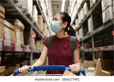 Asian Woman Wearing Protective Face Mask Pushing Shopping Cart, Choosing New Furniture In Big Store Warehouse. Shopping After Quarantine Due To Coronavirus Outbreak With New Normal Lifestyle 