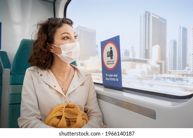 Asian woman wearing a protective face mask sits on a subway seat and looks hopefully out the window with Dubai views. The concept of the coronavirus and the covid-19 pandemic
