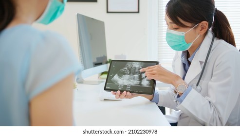 asian woman wearing protective face mask to prevent COVID19 has uterus utltrasonographic diagnosis in hospital - female doctor showing test results to patient on digital tablet