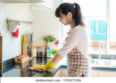 Asian Woman Wearing Rubber Protective Gloves Cleaning Kitchen Cupboards In Her Home During Staying At Home Using Free Time About Their Daily Housekeeping Routine.